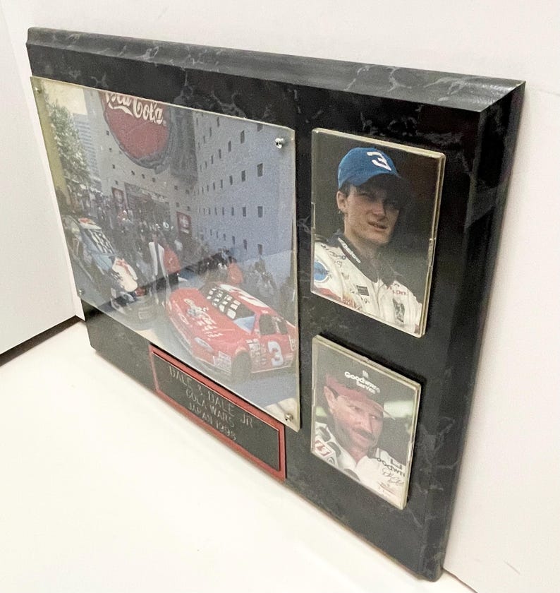 May include: A framed collage featuring racing imagery. The collage includes a large photo of a red race car with the number 3, a photo of a race car driver wearing a blue cap, and a photo of a race car driver wearing a red cap. The frame is black with a marble-like pattern.