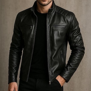 Op de afbeelding: Zwarte leren jas met een opstaande kraag en ritszakken. De jas heeft gewatteerde schouderdetails en een ritssluiting aan de voorkant. De persoon op de foto draagt een zwarte trui en een zwarte broek.