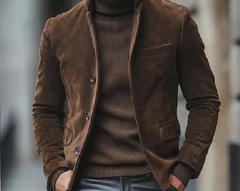 Op de afbeelding: Een bruin suède jasje met een opstaande kraag en twee voorzakken. De jas is dichtgeknoopt en wordt gedragen over een bruine coltrui. De persoon draagt ook een zwarte leren broek. De algehele look is stijlvol en verfijnd.