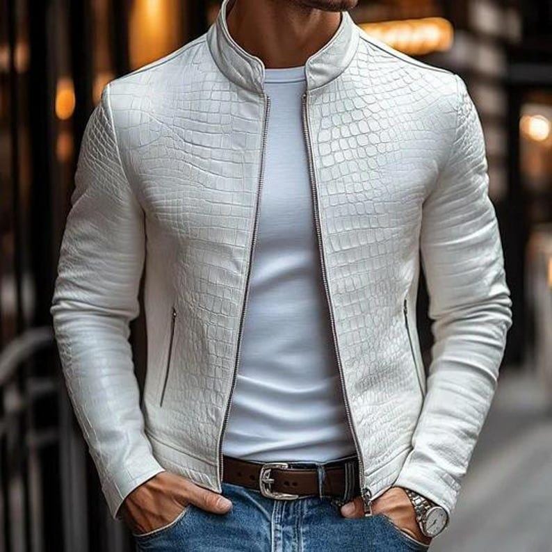 Peut inclure: Veste en cuir blanche textur&eacute;e avec un motif crocodile. La veste a un col montant, une fermeture &eacute;clair et deux poches lat&eacute;rales. La personne porte un t-shirt blanc, un jean bleu et une ceinture marron.