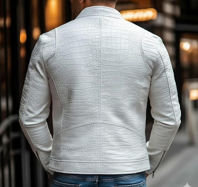 Peut inclure: Veste blanche &agrave; effet peau de crocodile. Elle pr&eacute;sente un col montant, des manches longues et une fermeture &eacute;clair sur la manche. L'image montre le dos de la veste, soulignant la texture et les d&eacute;tails du design.