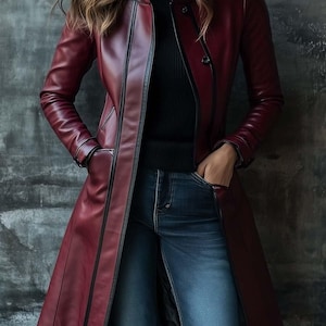 Peut inclure: Un long manteau en cuir bordeaux avec des bordures noires. Le manteau a une coupe ajustée, un col montant et une fermeture à boutons. Le modèle porte un col roulé noir et un jean bleu.