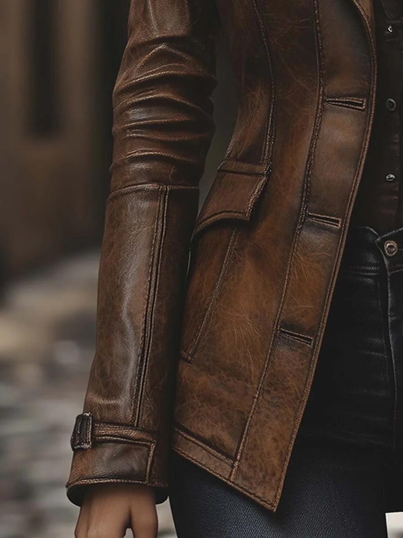 May include: A brown leather jacket with a classic design. The jacket has a notched collar, two front pockets, and button closures. The sleeves have a cuff detail with a buckle. The leather has a distressed appearance.