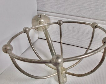 Puede incluir: Un soporte de pared de metal plateado con un diseño circular y múltiples puntos redondeados. El soporte está diseñado para sostener artículos como un cepillo de dientes u otros accesorios de baño.