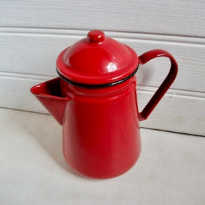 May include: Red enamel coffee pot with a black rim and a lid. The pot has a spout and a handle.