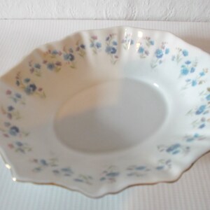 May include: White porcelain serving dish with a scalloped edge and a delicate floral pattern in blue, pink, and yellow. The rim is trimmed with gold. A classic piece for serving appetizers or desserts.