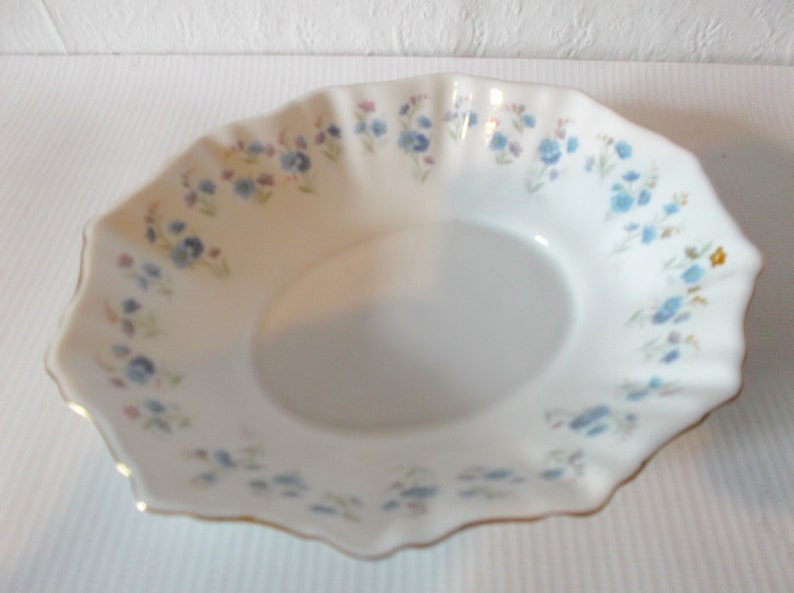 May include: White porcelain serving dish with a scalloped edge and a delicate floral pattern in blue, pink, and yellow. The rim is trimmed with gold. A classic piece for serving appetizers or desserts.
