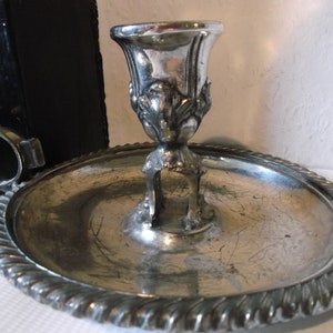 May include: Silver candlestick with a decorative base and a round tray with a rope-like edge.