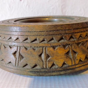 May include: A wooden bowl with a carved design. The bowl is brown and has a circular shape. The design is intricate and features a repeating pattern of stars.