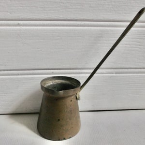 May include: A vintage copper coffee pot with a long handle. The pot is tarnished and has a rustic look.