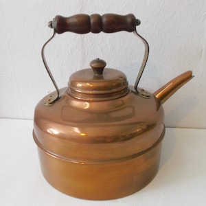 May include: A copper kettle with a wooden handle and a brass spout. The kettle has a shiny, polished finish.