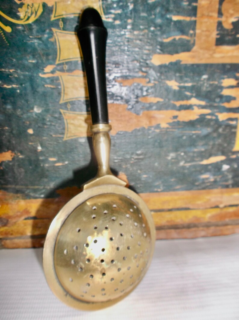 May include: A brass tea strainer with a black plastic handle. The strainer has a round, perforated bowl and a long, slender handle.