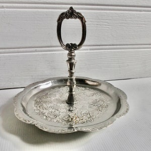 May include: A silver serving tray with a decorative handle. The tray has a scalloped edge and an ornate design.