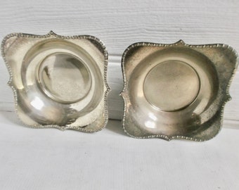 May include: Two silver serving dishes with scalloped edges and a beaded rim. The dishes are empty and have a reflective surface.