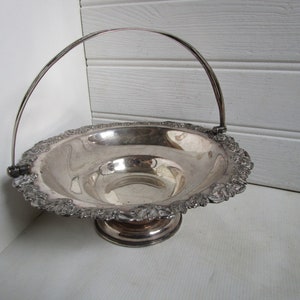 Puede incluir: Un plato de servir de plata con un borde decorativo y un asa. El plato tiene una base de pedestal y está hecho de metal pulido.