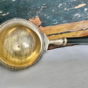 May include: A silver tea strainer with a black handle. The strainer has a round, perforated bowl with a decorative rim.