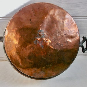 May include: A large, round copper pot with two black iron handles. The pot has a worn, aged appearance with a patina on the copper surface.