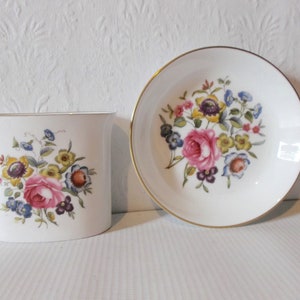 Może przedstawiać: Zestaw dwóch białych ceramicznych talerzy z kwiatowym wzorem. Talerze mają złotą obwódkę i przedstawiają bukiet różowych, żółtych i niebieskich kwiatów.
