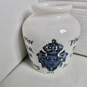 以下が含まれることがあります： 青と黒のペイントで装飾された白い陶器の壺。壺には王冠とユリの花の紋章が描かれています。壺には「Moulin de Poivre」と書かれています。