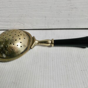 May include: A vintage silver tea strainer with a black plastic handle. The strainer has a round, perforated bowl and a long, slender handle.