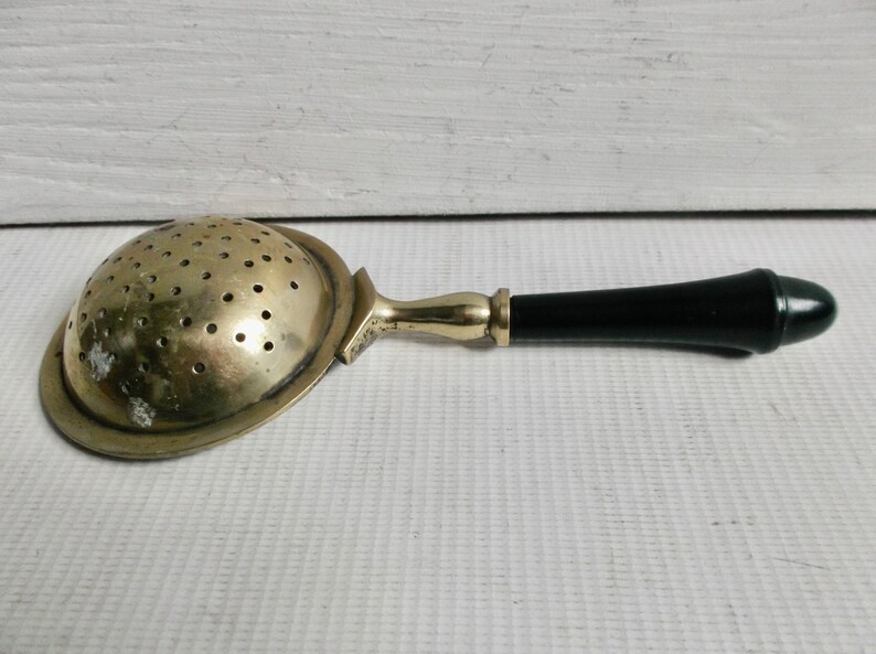 May include: A vintage silver tea strainer with a black plastic handle. The strainer has a round, perforated bowl and a long, slender handle.