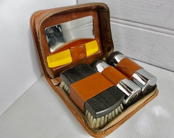 Puede incluir: Un estuche de viaje de cuero marrón con cierre de cremallera. El estuche contiene dos botellas de color plateado y marrón, un cepillo amarillo, un cepillo negro y marrón y un pequeño espejo.
