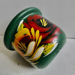 Könnte beinhalten: Ein kleiner grüner Keramiktopf mit einem floralen Design, das auf die Seite gemalt ist. Die Blumen sind rot, gelb und weiß.