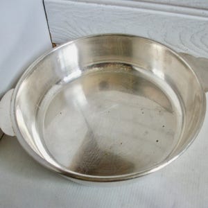 Puede incluir: Una fuente plateada brillante, de forma redonda, con dos asas decorativas. La fuente tiene poca profundidad y una superficie lisa y reflectante, ideal para servir alimentos.