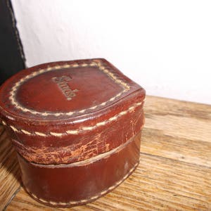 Puede incluir: Una caja de cuero marr&oacute;n con un borde cosido y la palabra "Swiss" en relieve en la parte superior.
