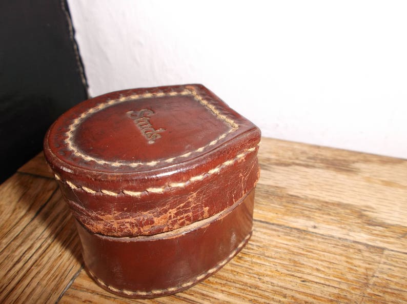Puede incluir: Una caja de cuero marr&oacute;n con un borde cosido y la palabra "Swiss" en relieve en la parte superior.