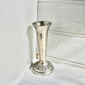 May include: A silver vase with a decorative base. The vase is tall and slender with a round base.