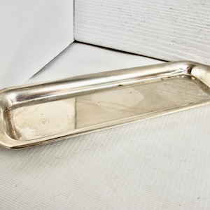 Puede incluir: Una bandeja rectangular de color plateado con bordes suavemente curvados. La bandeja tiene un borde ligeramente elevado y una superficie lisa y reflectante. Las esquinas son suavemente redondeadas y el diseño general es simple y elegante. Ideal para servir o exhibir.