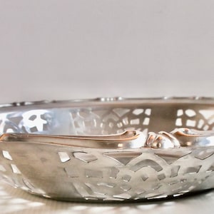 May include: A silver serving bowl with an intricate, openwork design. The bowl has a scalloped edge and a slightly rounded bottom.