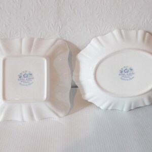 May include: Two white porcelain dishes with ruffled edges. One is square, the other oval. Both have a floral design and the words "Royal Albert Bone China, Harmony Light" printed on the bottom.