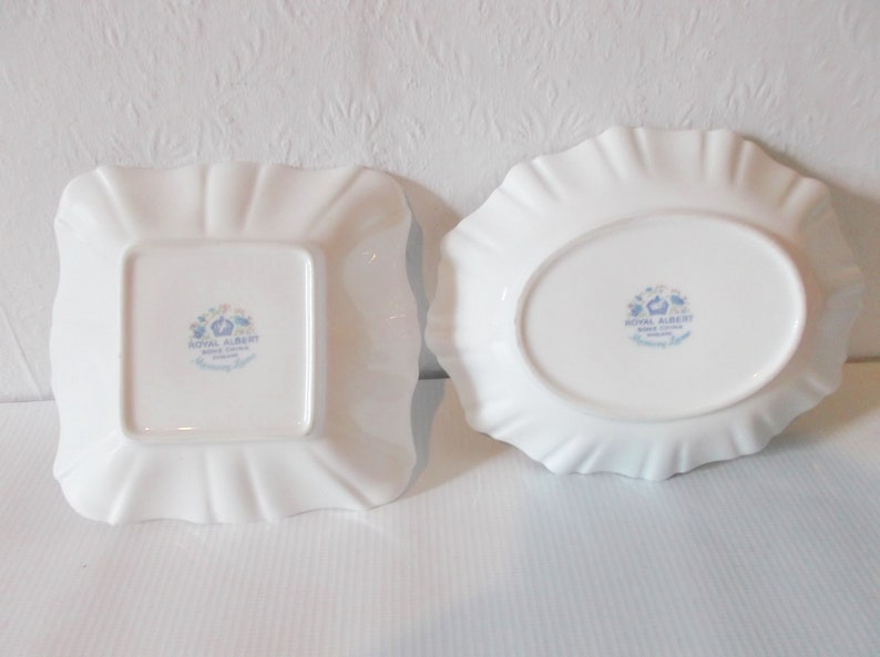 May include: Two white porcelain dishes with ruffled edges. One is square, the other oval. Both have a floral design and the words "Royal Albert Bone China, Harmony Light" printed on the bottom.