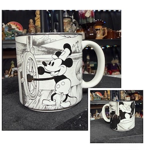 May include: White ceramic mug with a black and white illustration of Mickey Mouse steering a ship. The mug has a large, curved handle and a black rim. The design wraps around the mug.