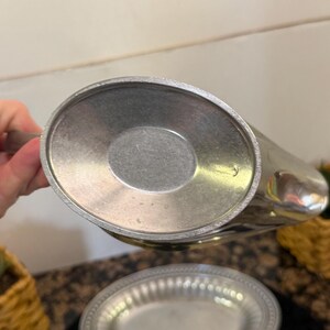 May include: The underside of a metallic gravy boat featuring a smooth, oval-shaped base with a slightly recessed center. The surface has a matte, brushed silver-tone finish with a visible circular texture pattern consistent with metal casting.
