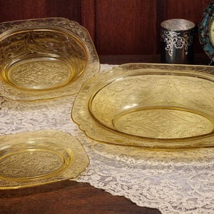 May include: Three pieces of amber-colored Depression glass tableware. The set includes a large oval serving dish, a smaller oval bowl, and a rectangular plate. All pieces have a detailed floral pattern.