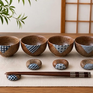 May include: A set of four round, speckled brown ceramic bowls and four matching circular chopstick rests, each featuring a unique blue and white geometric pattern accent. A pair of dark brown wooden chopsticks with silver-toned metal bands.