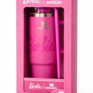 May include: A pink Stanley tumbler with the Barbie logo in a pink box. The tumbler has a handle and a gold rim. The box also features the Barbie and Stanley logos.