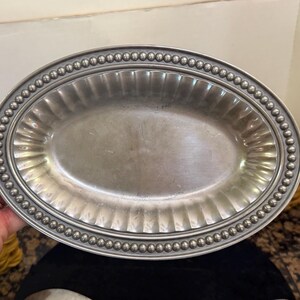 May include: An oval-shaped silver-toned metal serving platter featuring a smooth central basin, a wide fluted rim, and a decorative border composed of a continuous row of small, raised spherical beads along the outer edge of the tray.