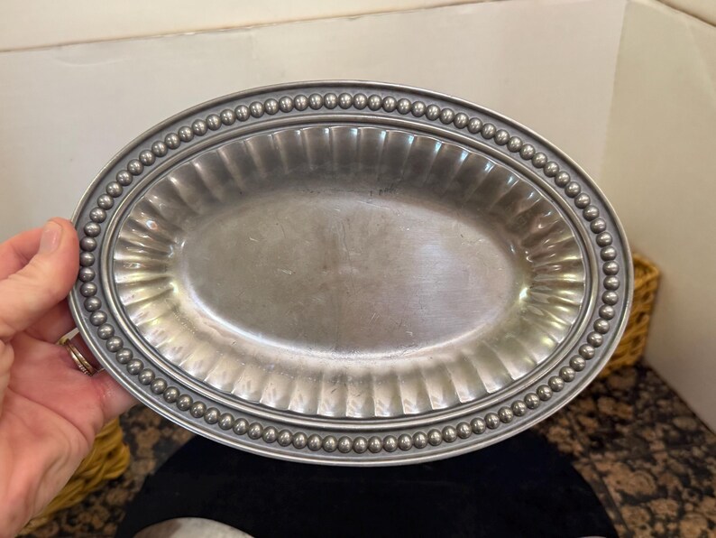 May include: An oval-shaped silver-toned metal serving platter featuring a smooth central basin, a wide fluted rim, and a decorative border composed of a continuous row of small, raised spherical beads along the outer edge of the tray.
