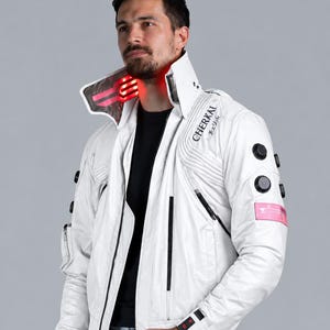 Könnte beinhalten: Eine weiße Jacke mit hohem Kragen und integrierten roten LED-Lichtern. Die Jacke verfügt über schwarze kreisförmige Akzente an den Ärmeln, einen rosafarbenen rechteckigen Aufnäher und den Schriftzug CHERKAI mit japanischen Zeichen.