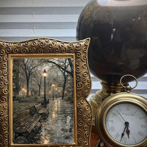 Puede incluir: Un cuadro dorado enmarcado de una escena de parque con bancos y farolas. También se ven un jarrón decorativo y un pequeño reloj de latón con números romanos. El marco tiene un diseño ornamental y ondulado.