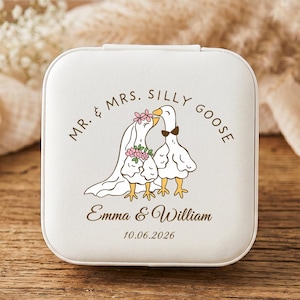 May include: A square white jewelry box featuring a printed illustration of two geese dressed for a wedding. The text reads MR. & MRS. SILLY GOOSE, Emma & William, and the date 10.06.2026. The geese wear a veil, flower crown, and bow tie.