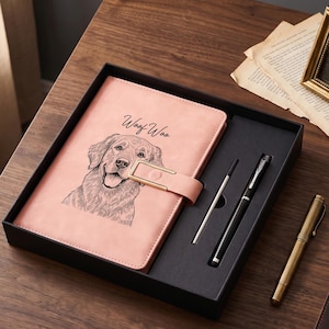 Puede incluir: Un cuaderno rosa con un cierre dorado y un dibujo lineal en negro de la cara de un perro, con el texto "Woof Woo" sobre la ilustración. El cuaderno se presenta en una caja de regalo negra junto a un bolígrafo negro y un recambio plateado.