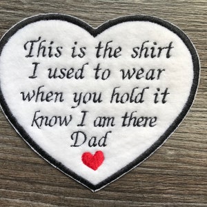 Peut inclure: Patch en forme de cœur blanc avec des coutures noires autour des bords. Le patch a un texte brodé noir qui dit "This is the shirt I used to wear when you hold it know I am there Dad". Un petit cœur rouge est brodé en bas du patch.
