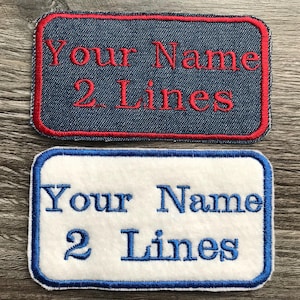 May include: Two rectangular embroidered patches with blue stitching. The top patch is denim blue with red stitching and the text "Your Name 2 Lines" in red. The bottom patch is white with blue stitching and the text "Your Name 2 Lines" in blue.