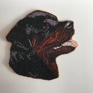 Puede incluir: Parche bordado de la cabeza de un perro Rottweiler, el perro está mirando hacia la derecha, el parche es marrón, negro y blanco.