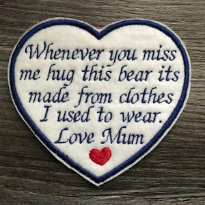 May include: A white heart-shaped patch with a blue border and embroidered text. The text reads "Whenever you miss me hug this bear its made from clothes I used to wear. Love Mum." A small red heart is at the bottom.